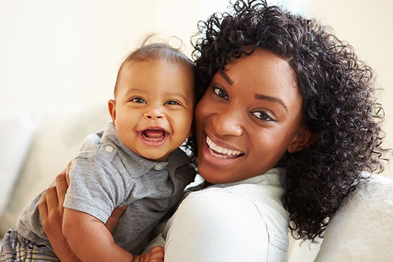 Smiling woman holding a laughing baby in a bright indoor setting