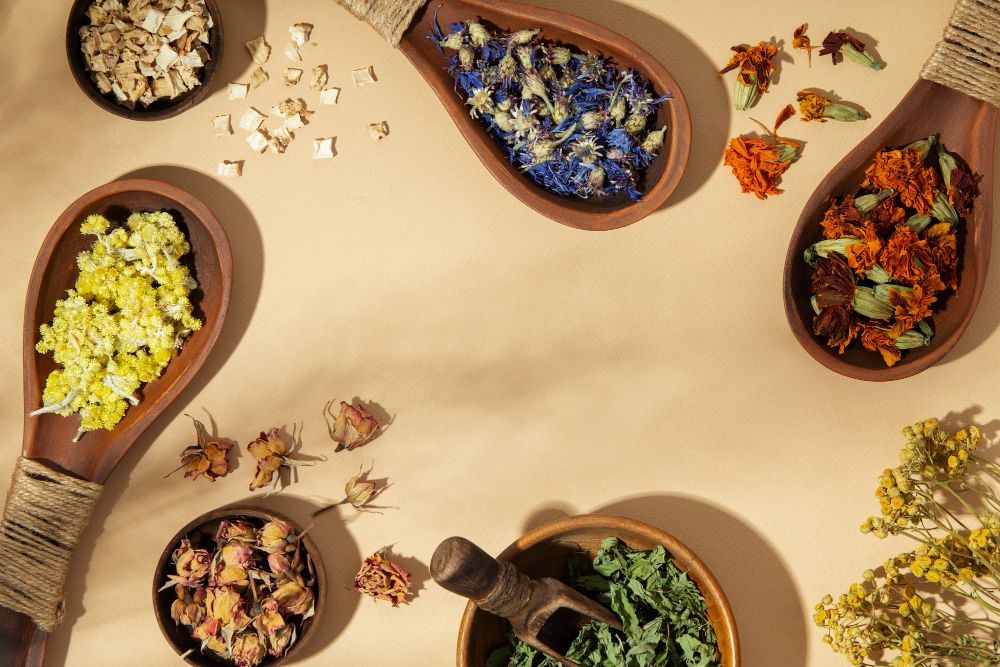 Overhead view of wooden bowls filled with dried flowers and petals on a beige background