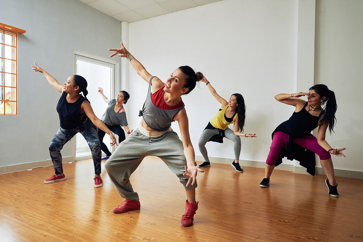 Five people dancing in a bright studio with wooden floors and white walls