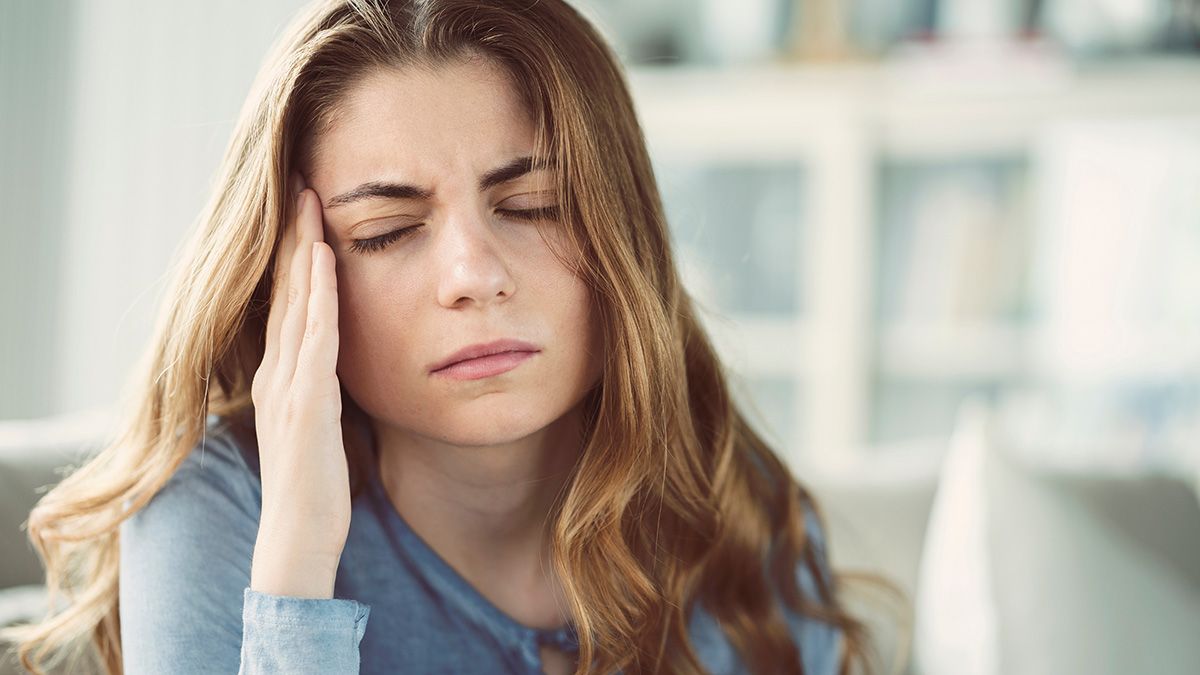 Woman holding her temple with eyes closed, looking tired or in pain indoors.