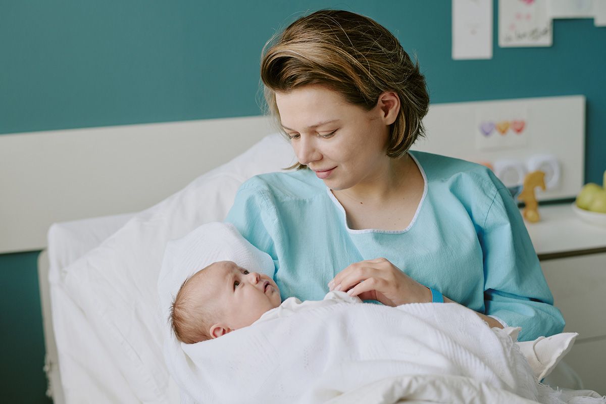Woman in a hospital bed smiling at her newborn baby wrapped in a white blanket