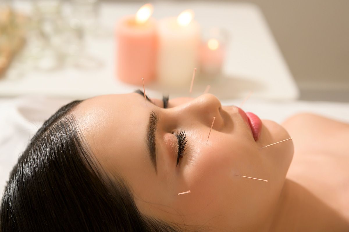 Person relaxing with eyes closed during a spa facial, with candles blurred in the background