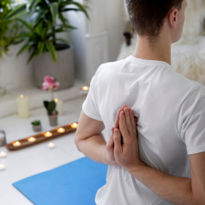 Person seated on a blue yoga mat in a calm room, reaching one hand behind their back during a stretch