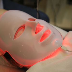 White LED face mask on a person lying down, glowing red in a spa setting