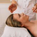 A massage therapist works on a woman lying face up on a white towel.
