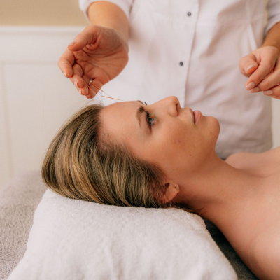 A massage therapist works on a woman lying face up on a white towel.