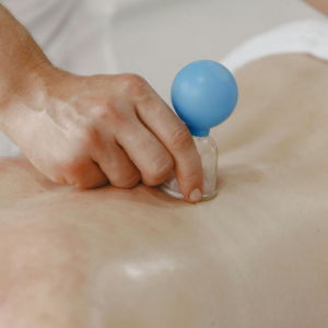 Hand pressing a small blue tool into a person's back during massage therapy