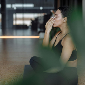 Person sitting on a mat, wiping sweat from their face in a gym or studio.