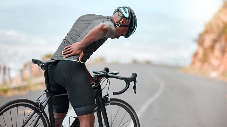 Cyclist in black gear bending over beside a road bike on a mountain road, resting after a ride