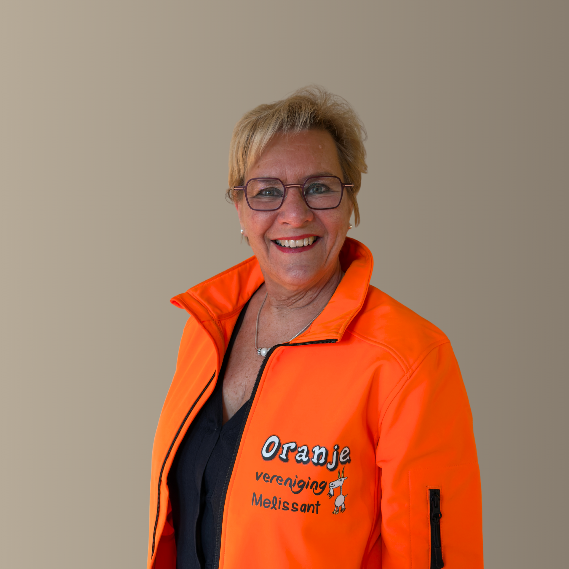 Vrouw in oranje jasje, lachend, met bril, staand. Op het jasje staat 