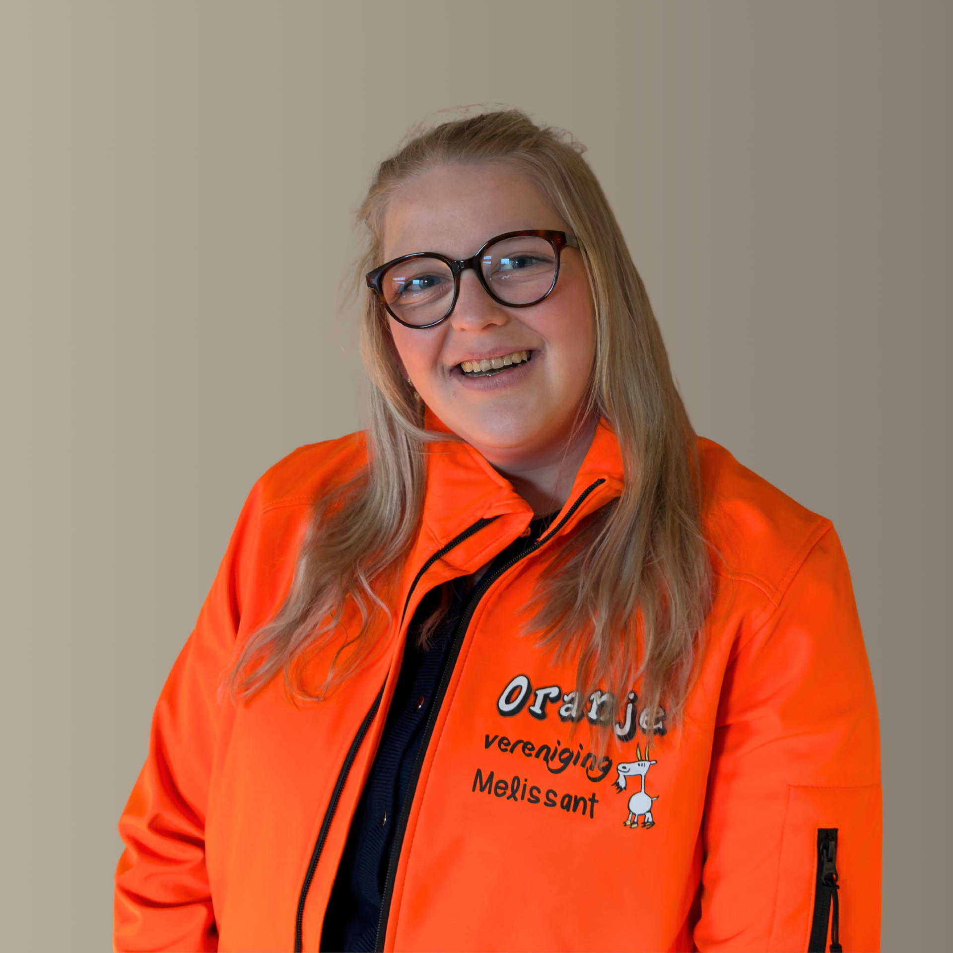 Vrouw in oranje jasje, met bril op en een glimlach, lichtjes voorovergebogen. Tegen een neutrale muur.