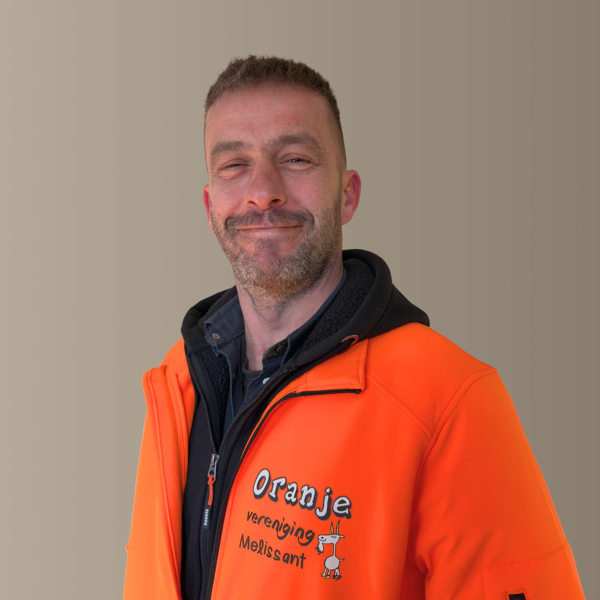 Man in orange jacket, smiling, jacket reads 