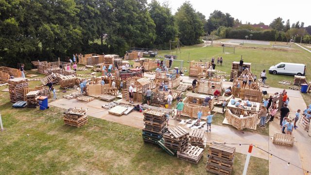 Mensen bouwen constructies van houten pallets in een park op een zonnige dag.