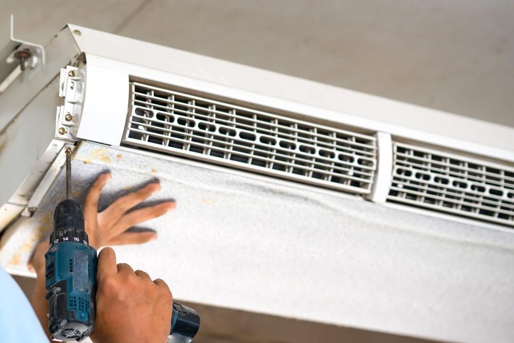 A Man Is Using A Drill To Fix An Air Conditioner — Custom Air In Yackandandah, NSW