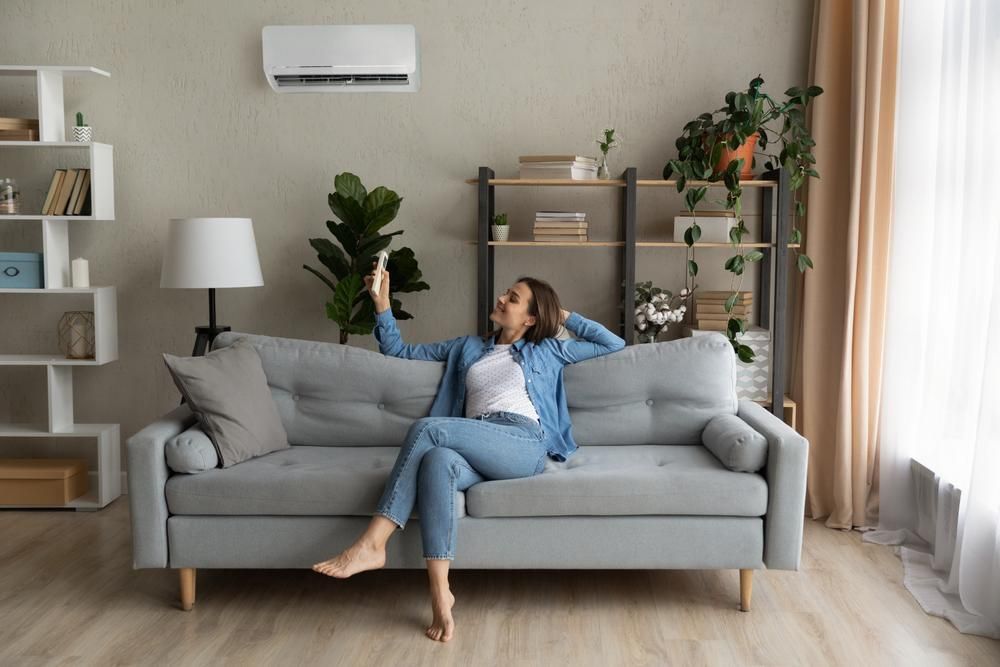 A Woman Is Sitting On A Couch In A Living Room Holding A Remote Control — Custom Air In East Albury, NSW