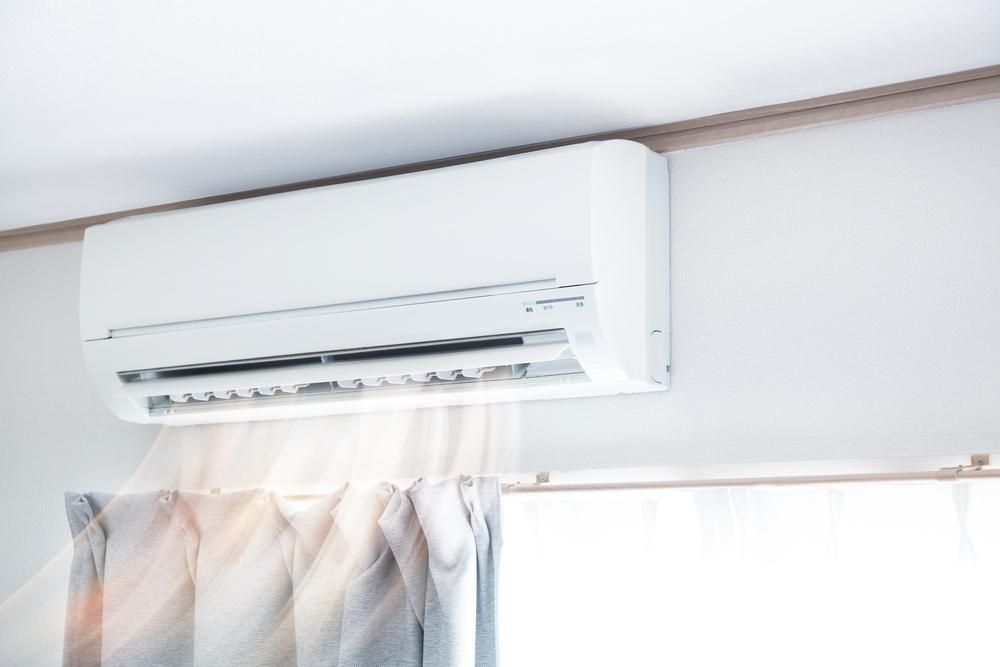 A White Air Conditioner Is Hanging From The Ceiling In A Room Next To A Window — Custom Air In Mount Beauty, NSW