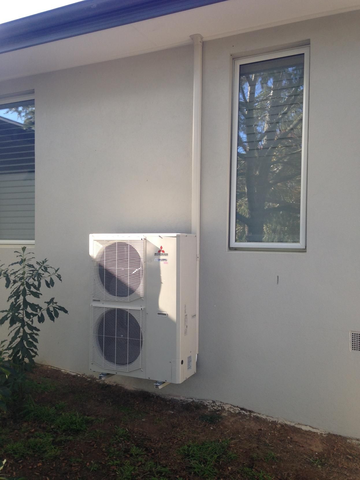 A Large Air Conditioner Is Mounted On The Side Of A House Next To A Window — Custom Air In East Albury, NSW