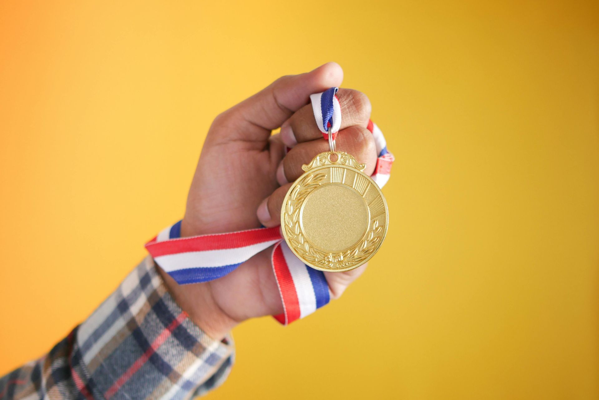 Close-up of a hand lifting a gold award medal on a ribbon, representing excellence and achievement.