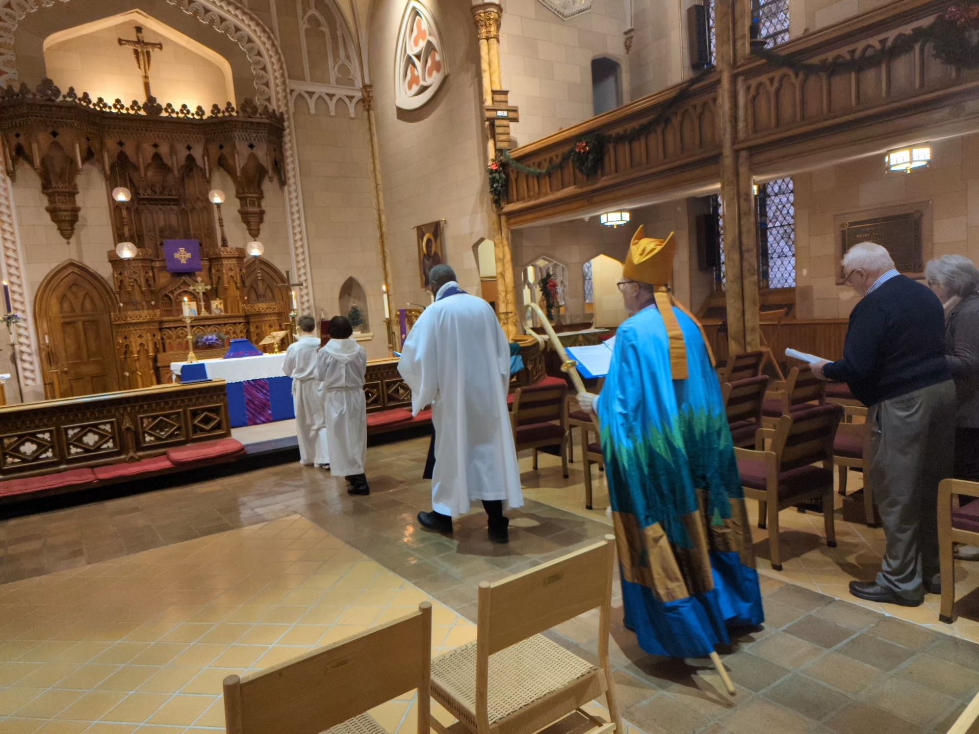 A bishop in blue and green vestments leads a church procession. Interior view.