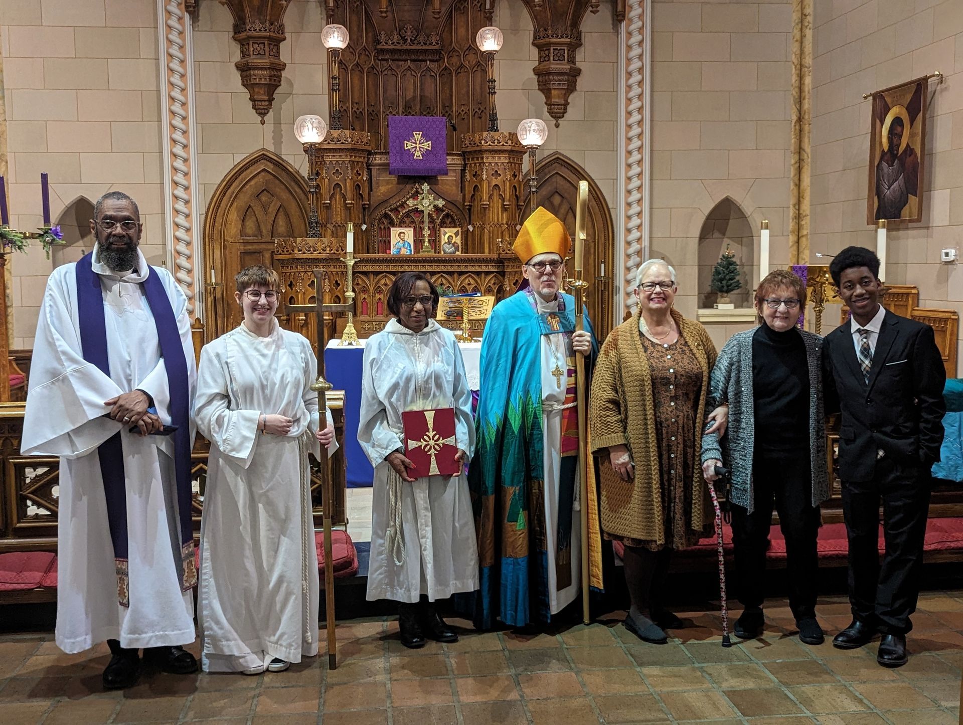 Group in church, clergy, and community members. Bishop in blue robes, standing in front of an altar.