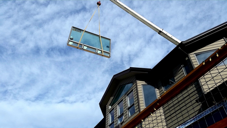 Construction crane lifting a large window into a building during installation on a commercial project.