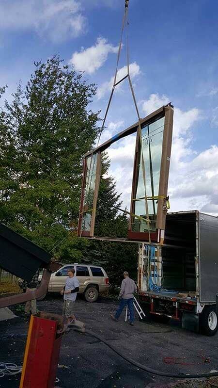 A crane lifting a large window into a truck during a construction logistics operation.