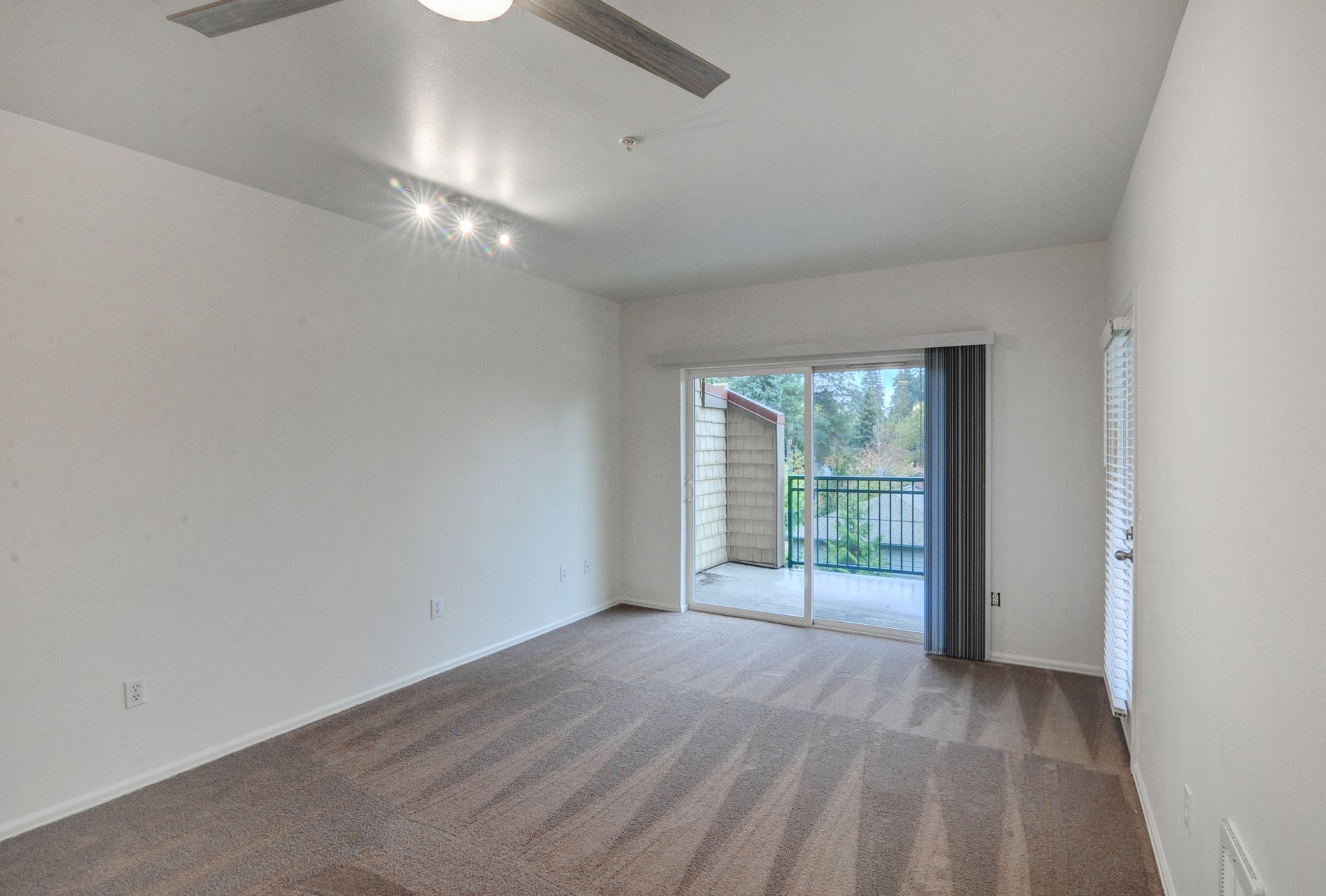 an empty living room with a ceiling fan and sliding glass doors leading to a balcony .