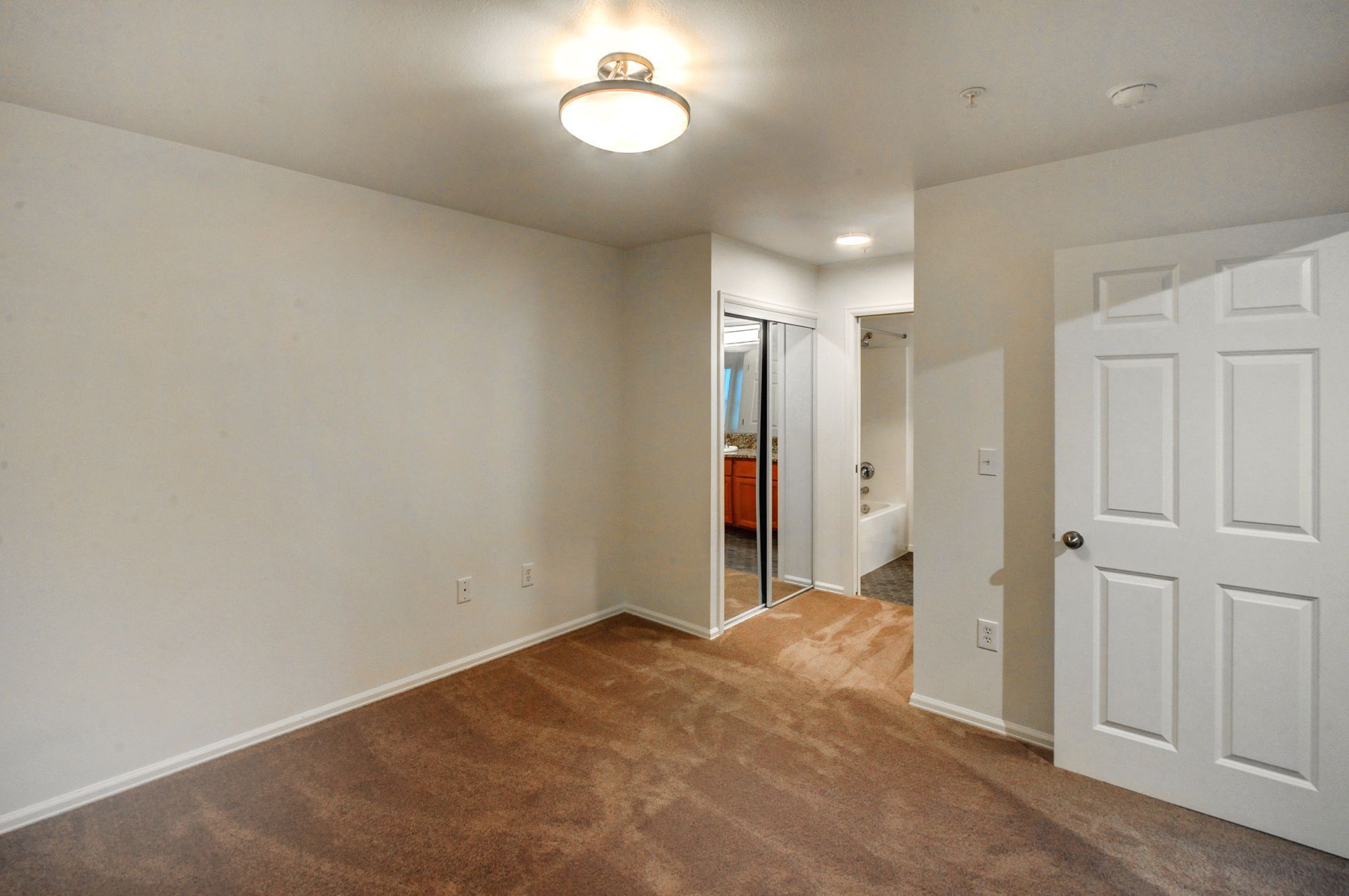 an empty bedroom with a brown carpet and a white door leading to a bathroom .