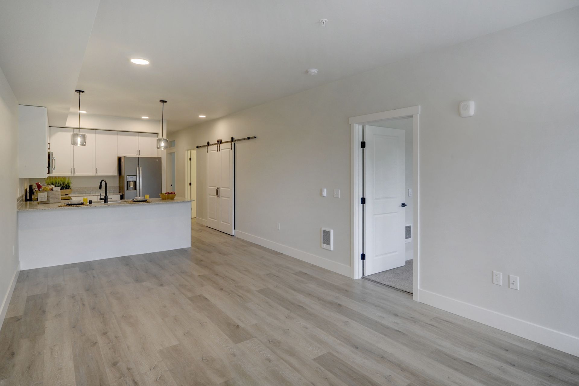 an empty living room with hardwood floors and a kitchen in the background .