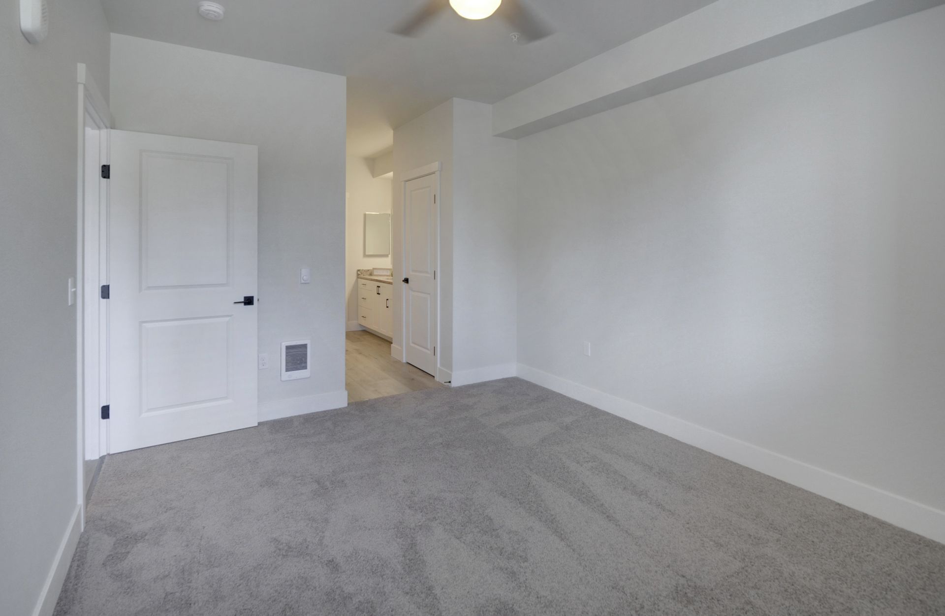 an empty bedroom with a ceiling fan and a gray carpet .