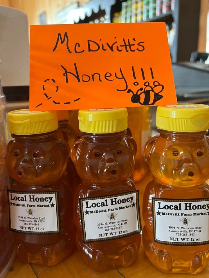 Bottles of local honey are lined up under an orange sign that says mcdivitt 's honey