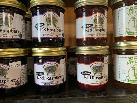 A shelf filled with jars of jam including black raspberry and red raspberry.