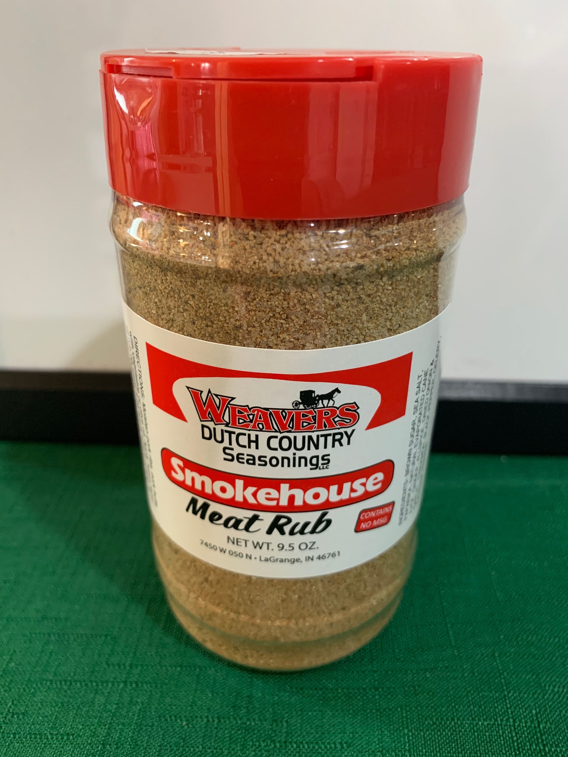A jar of smokehouse meat rub is sitting on a green table.