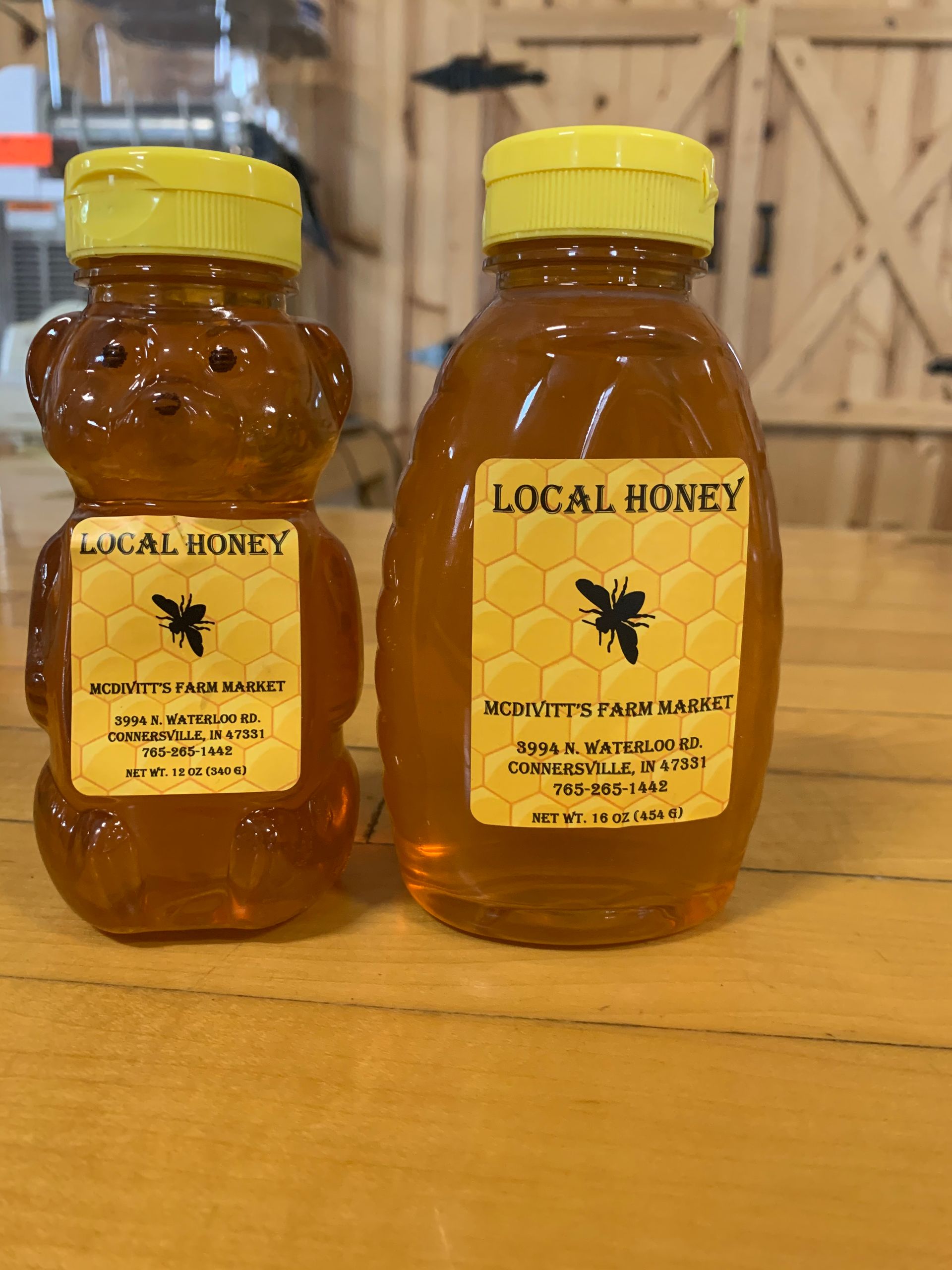 Two bottles of local honey are sitting on a wooden table.