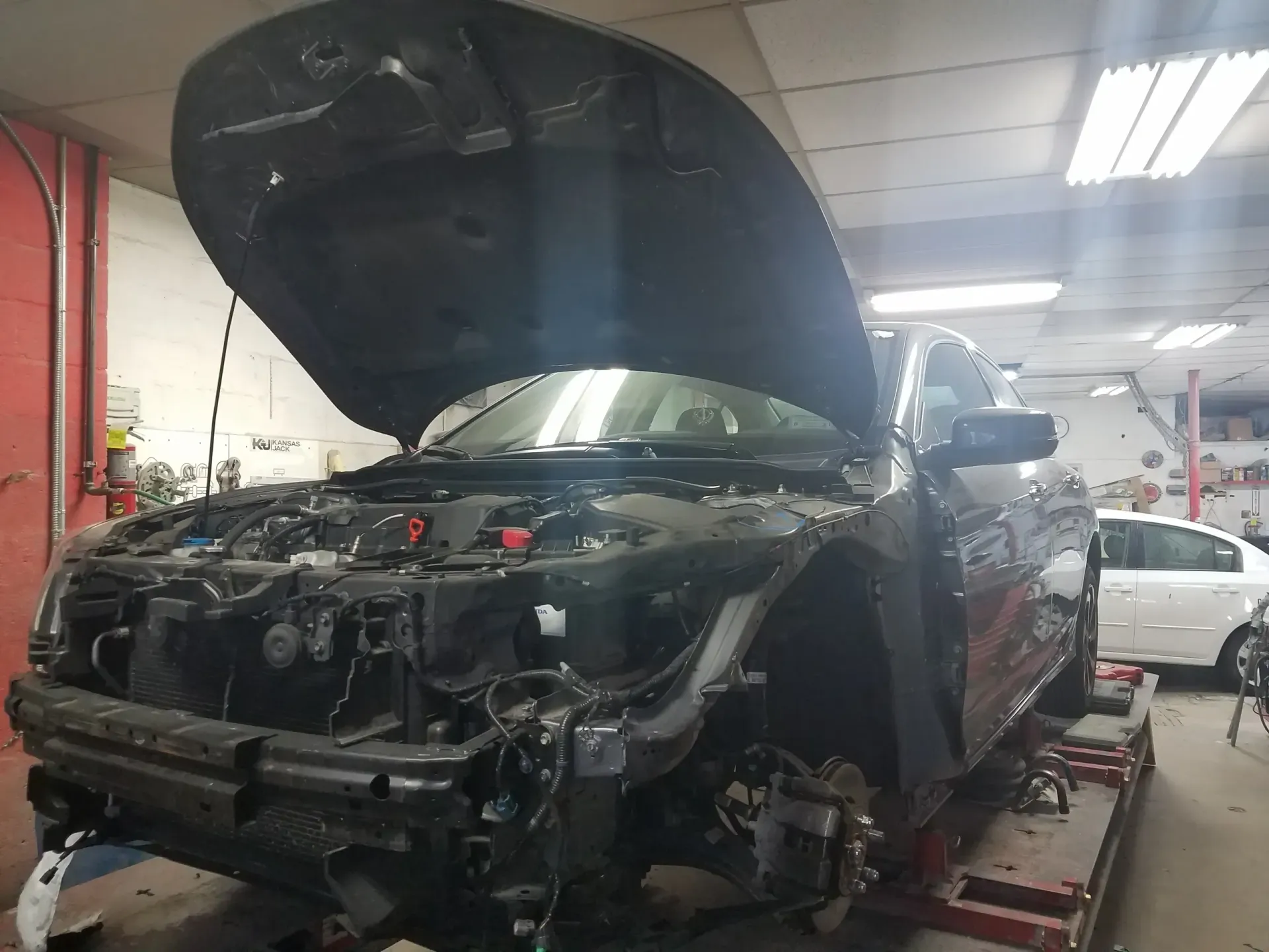 a car with the hood up is being worked on in a garage .