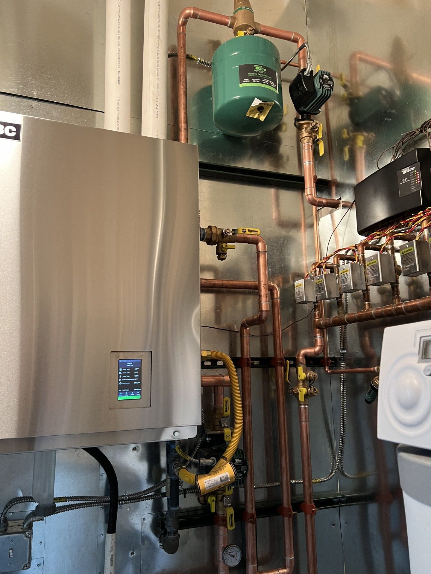 A stainless steel water heater is sitting in a room with copper pipes.
