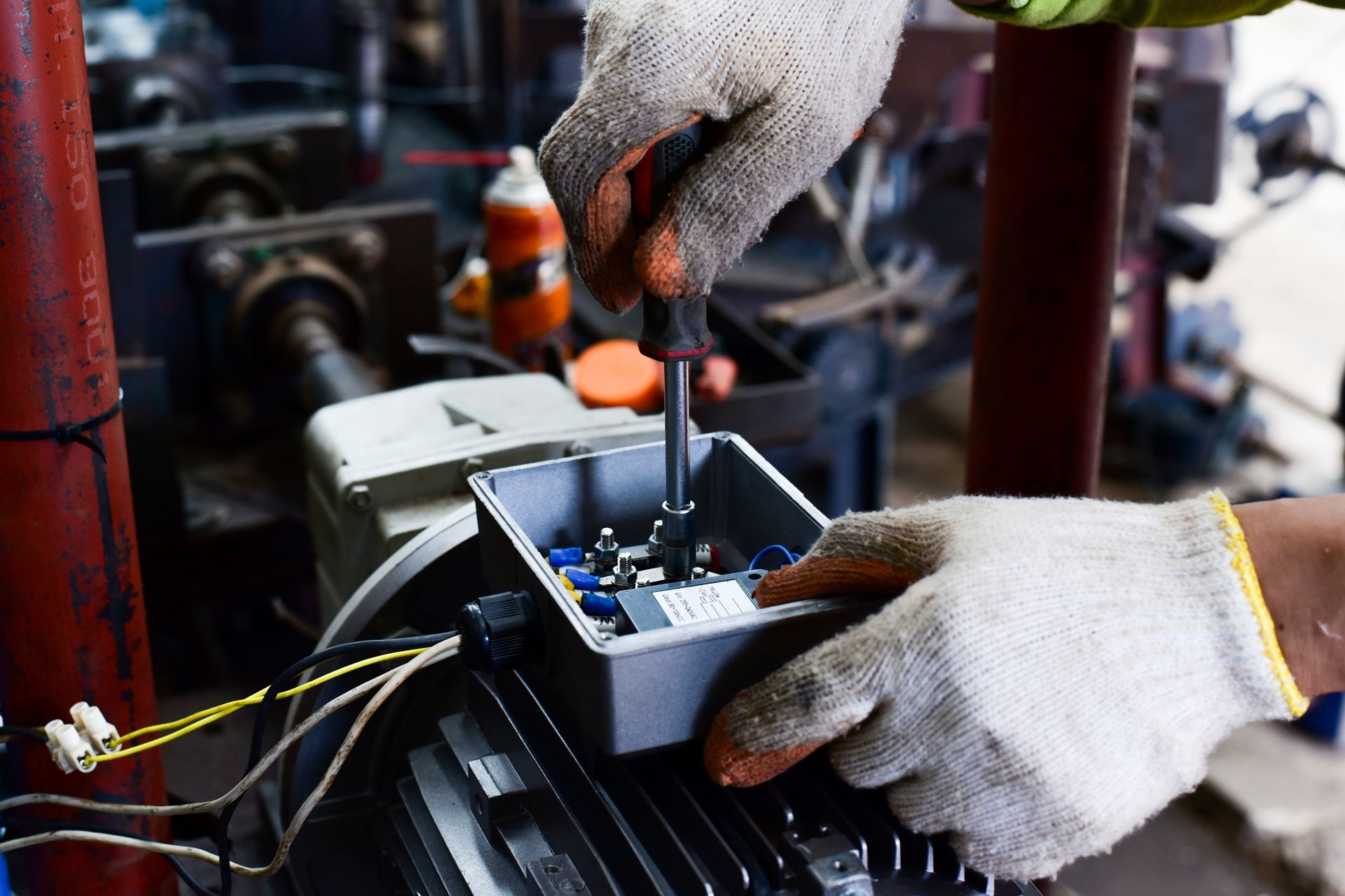 Hands in work gloves using a screwdriver to adjust an electrical component. Industrial setting.