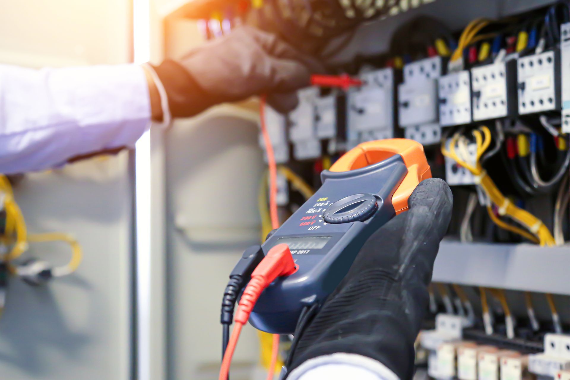 Person using a red multimeter to test electrical components in a gray control panel.