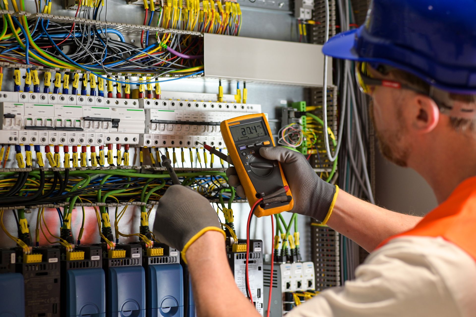 Electrician testing wiring with a multimeter inside a control panel.