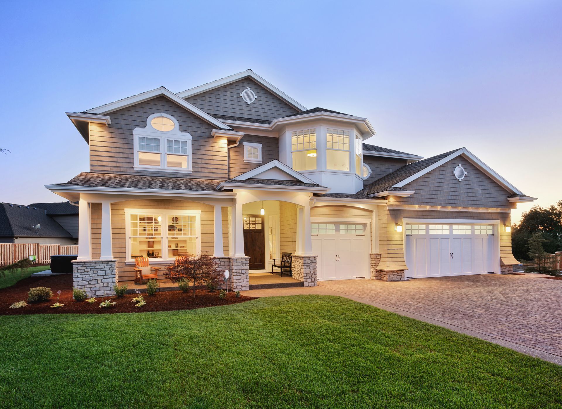 Two-story gray house with white trim, a gabled roof, and a green lawn at dusk.