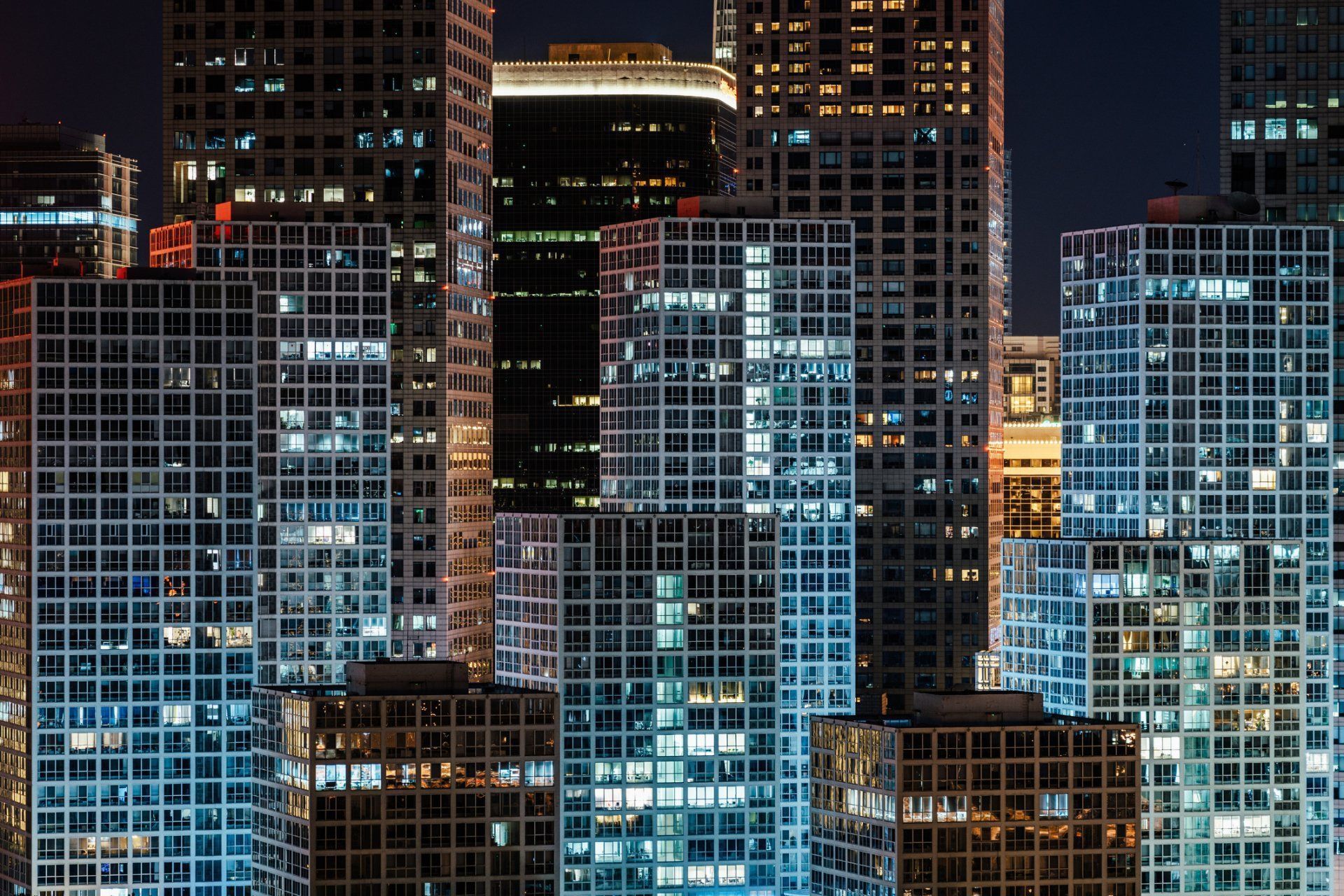 Illuminated skyscrapers at night with various blue and yellow window lights.