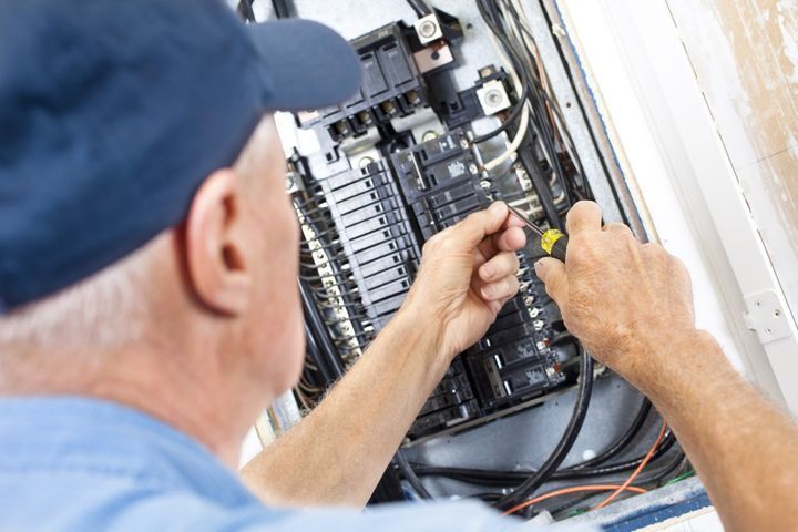 Electrician working on a circuit breaker panel with a screwdriver.