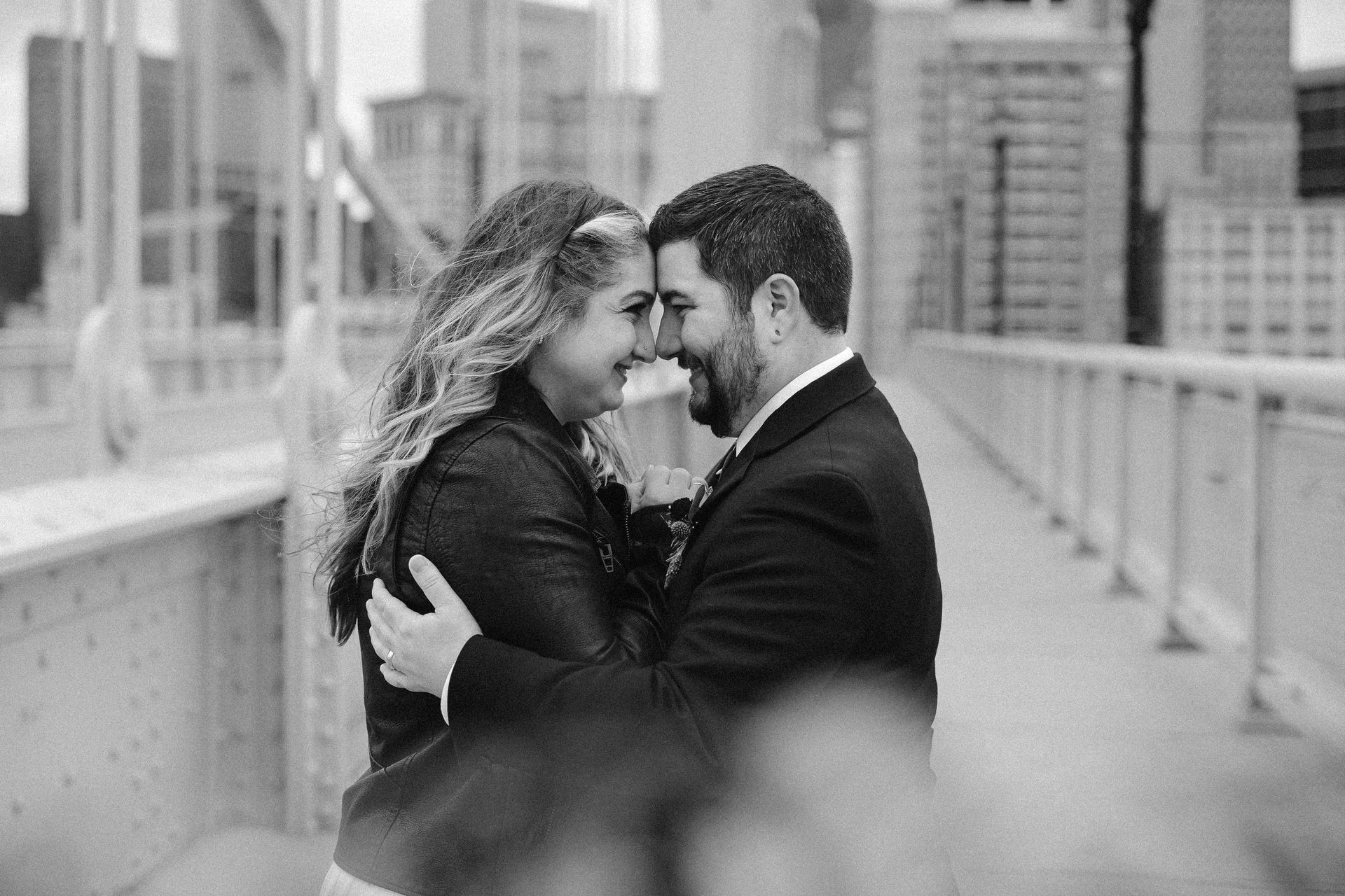 a black and white photo of a man and woman hugging each other on a bridge . natural wedding makeup. pittsburgh, pa. bridal makeup. bridal mua. wedding makeup artist. moriah e beauty. liz capuano photography.