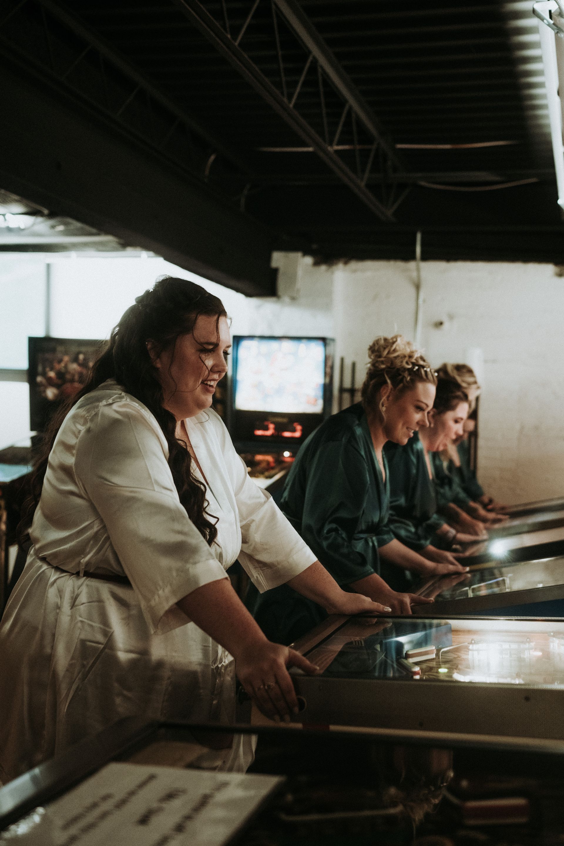 a bride and her bridesmaids are playing pinball machines . natural wedding makeup. pittsburgh, pa. bridal makeup. bridal mua. wedding makeup artist. moriah e beauty. carlie gabrelcik photography.