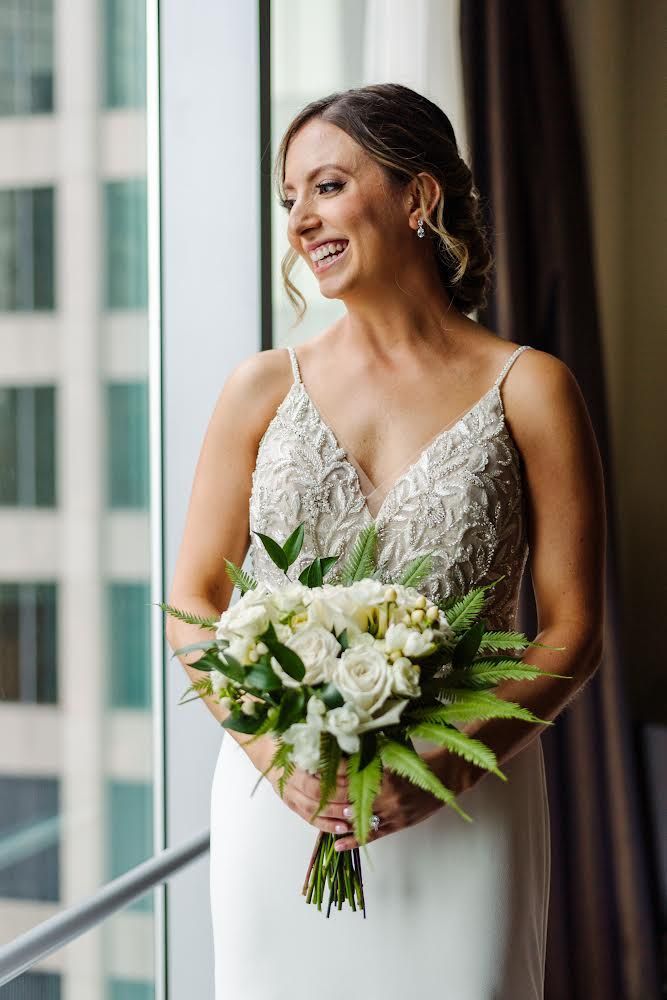 a bride in a wedding dress is holding a bouquet of flowers and looking out of a window . natural wedding makeup. pittsburgh, pa. bridal makeup. bridal mua. wedding makeup artist. moriah e beauty. michael will pro photo.