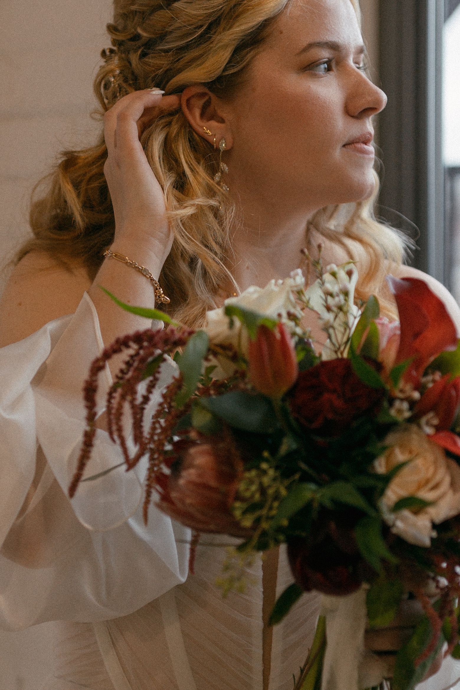 a bride is putting on her earrings while holding a bouquet of flowers . natural wedding makeup. pittsburgh, pa. bridal makeup. bridal mua. wedding makeup artist. moriah e beauty. hannah conti photography.