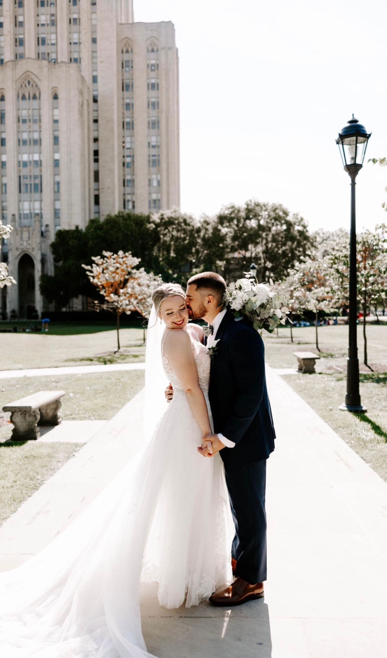 a bride and groom are kissing on a sidewalk in front of a building . natural wedding makeup. pittsburgh, pa. bridal makeup. bridal mua. wedding makeup artist. moriah e beauty. rachel wehan photography.