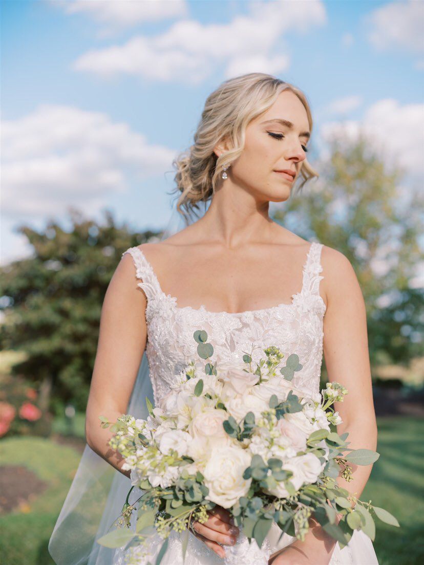 a bride in a wedding dress is holding a bouquet of white flowers . natural wedding makeup. pittsburgh, pa. bridal makeup. bridal mua. wedding makeup artist. moriah e beauty. anna laero photography.