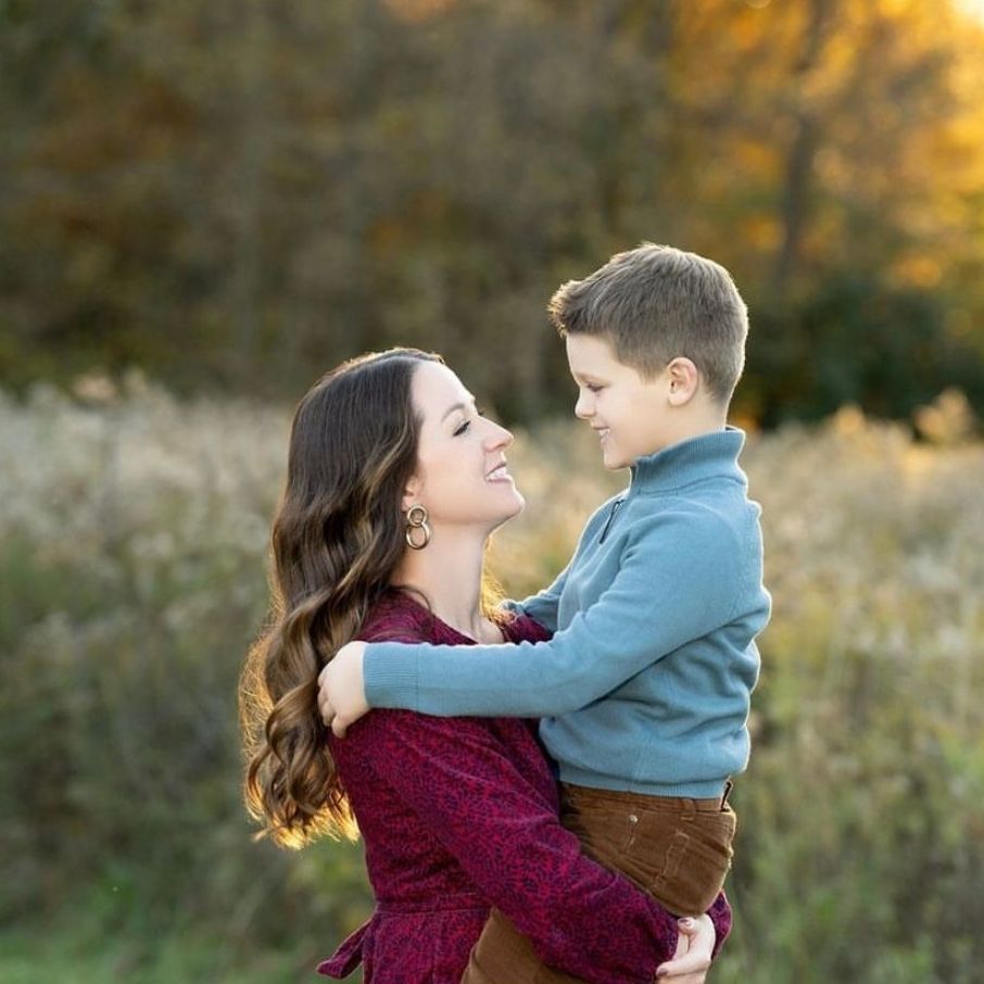 a woman is holding a boy in her arms in a field . natural makeup. pittsburgh, pa. family photos makeup. bridal mua. wedding makeup artist. moriah e beauty. kristin merck photography.