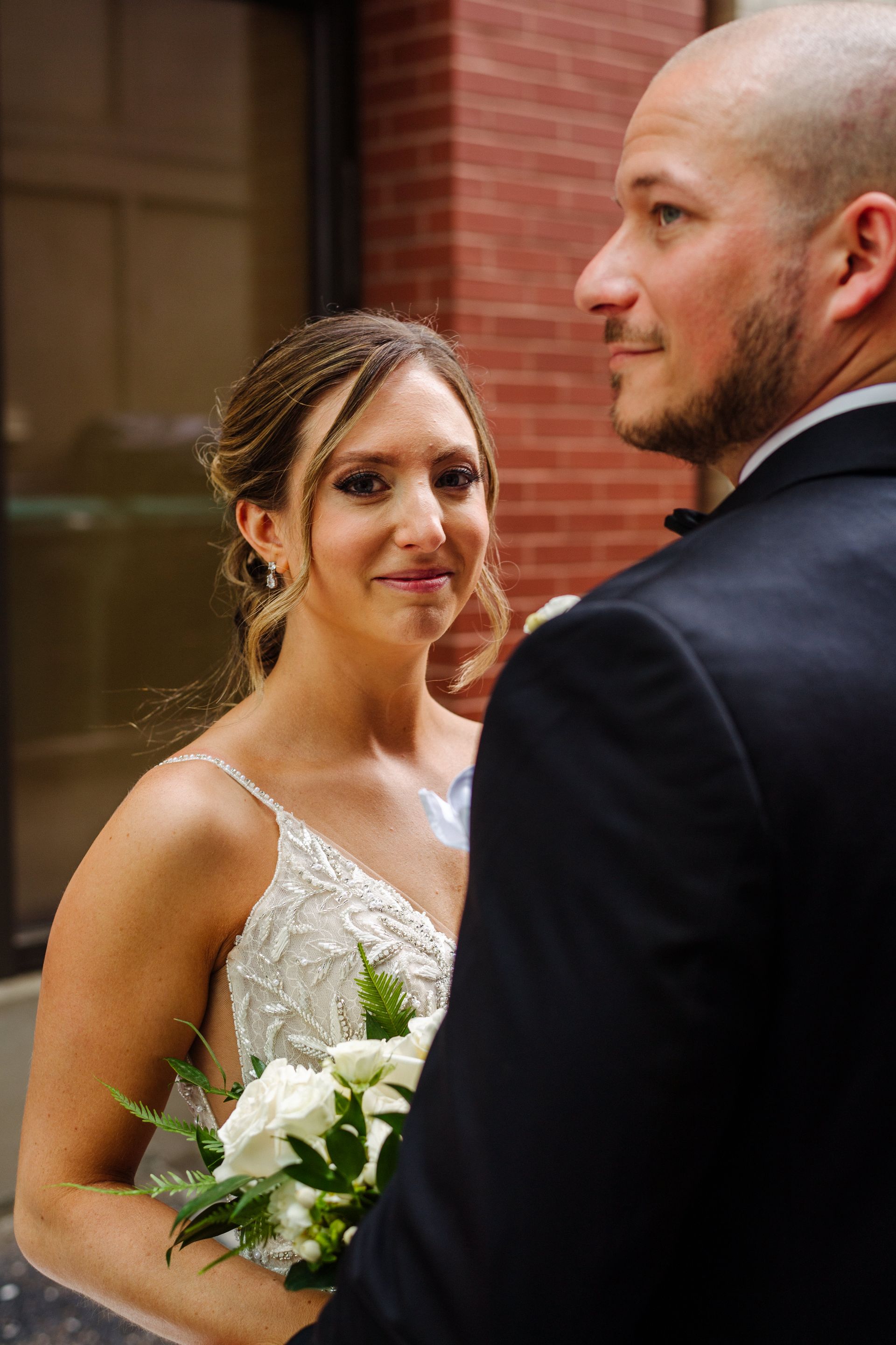 a bride and groom are standing next to each other in front of a brick building . natural wedding makeup. pittsburgh, pa. bridal makeup. bridal mua. wedding makeup artist. moriah e beauty. michael will pro photo.